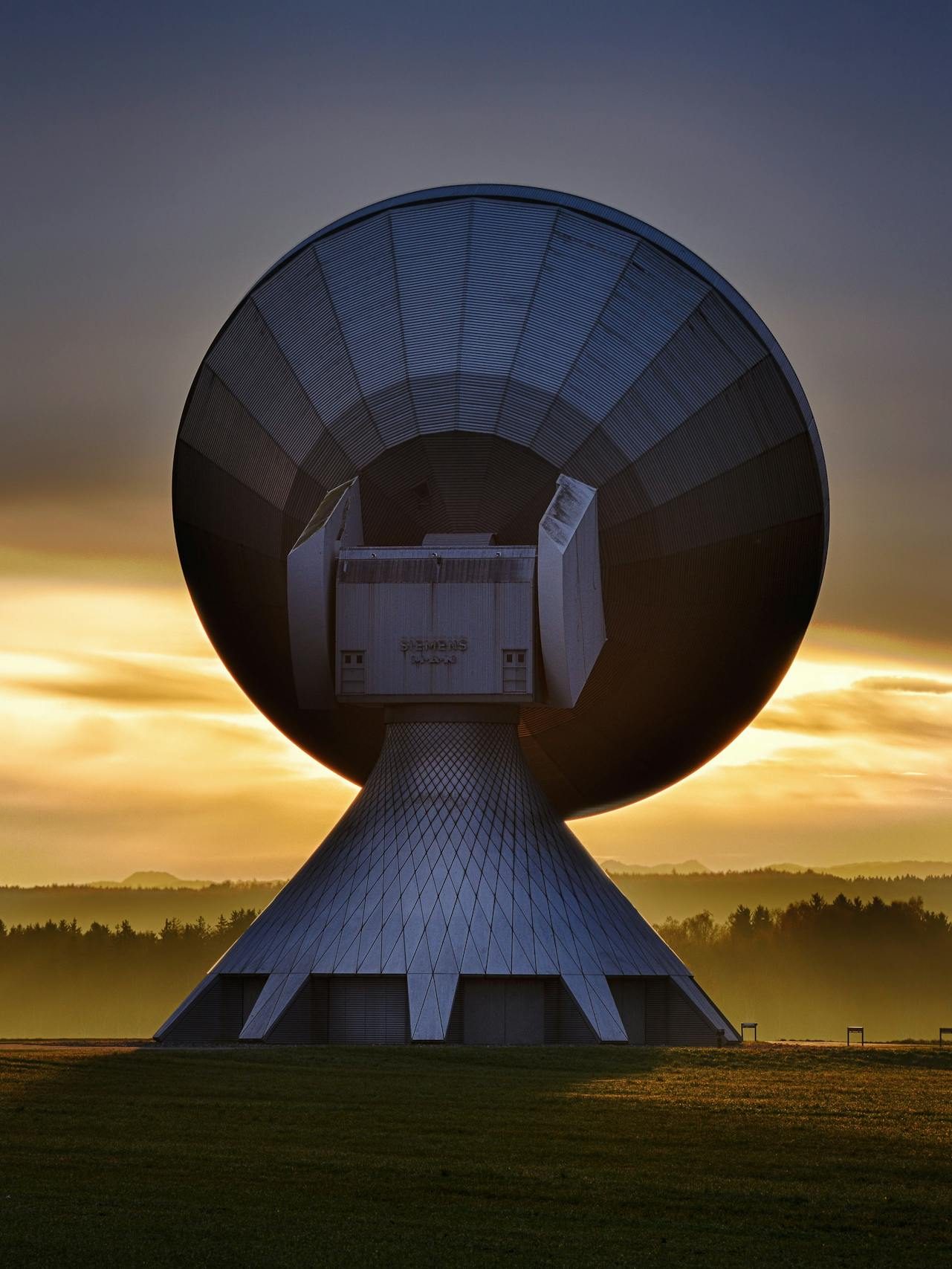 Large satellite dish silhouette against a colorful sunset, showcasing broadcasting technology.